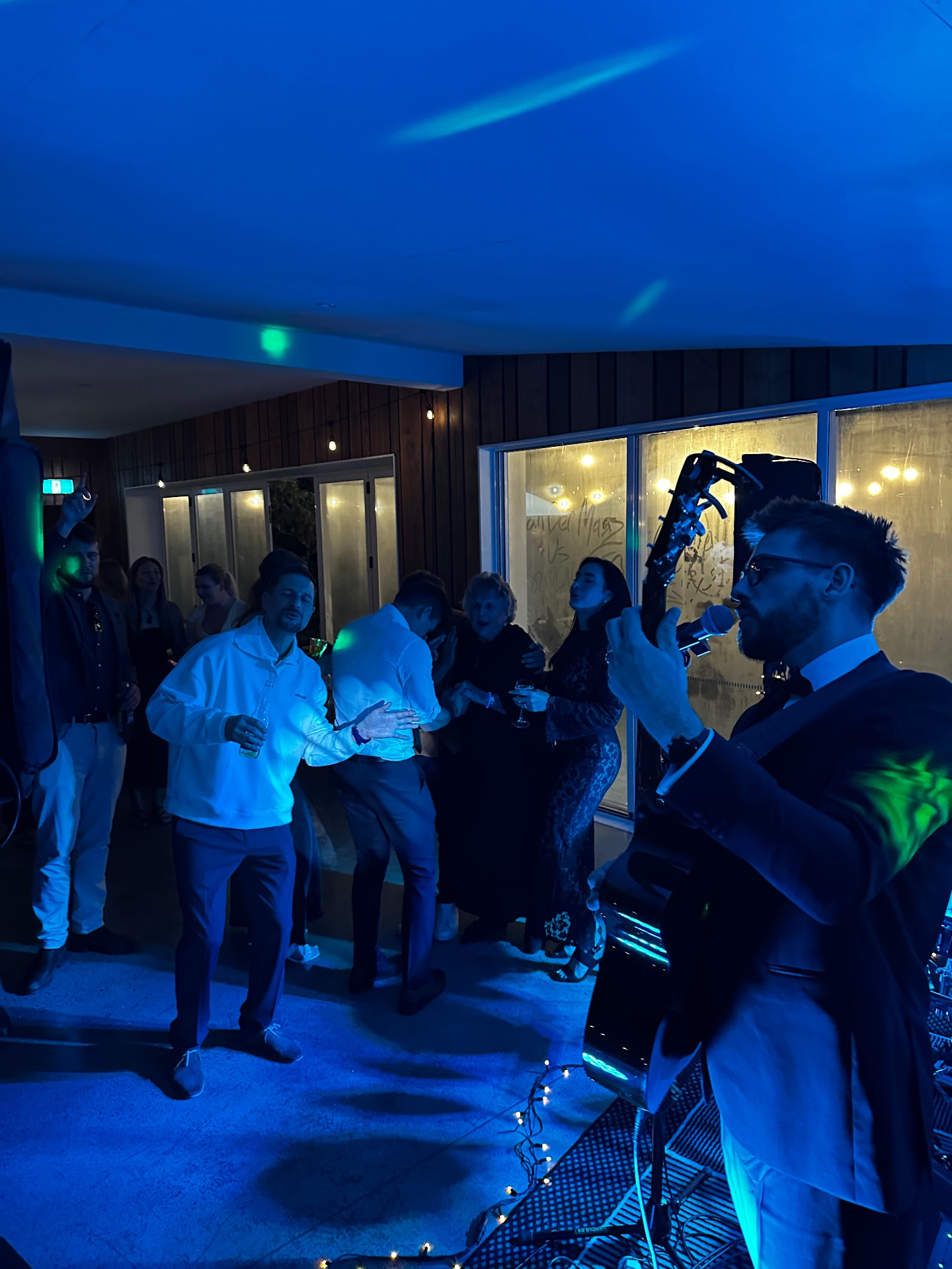 James Van playing guitar and singing at a wedding reception with guests dancing under blue lights